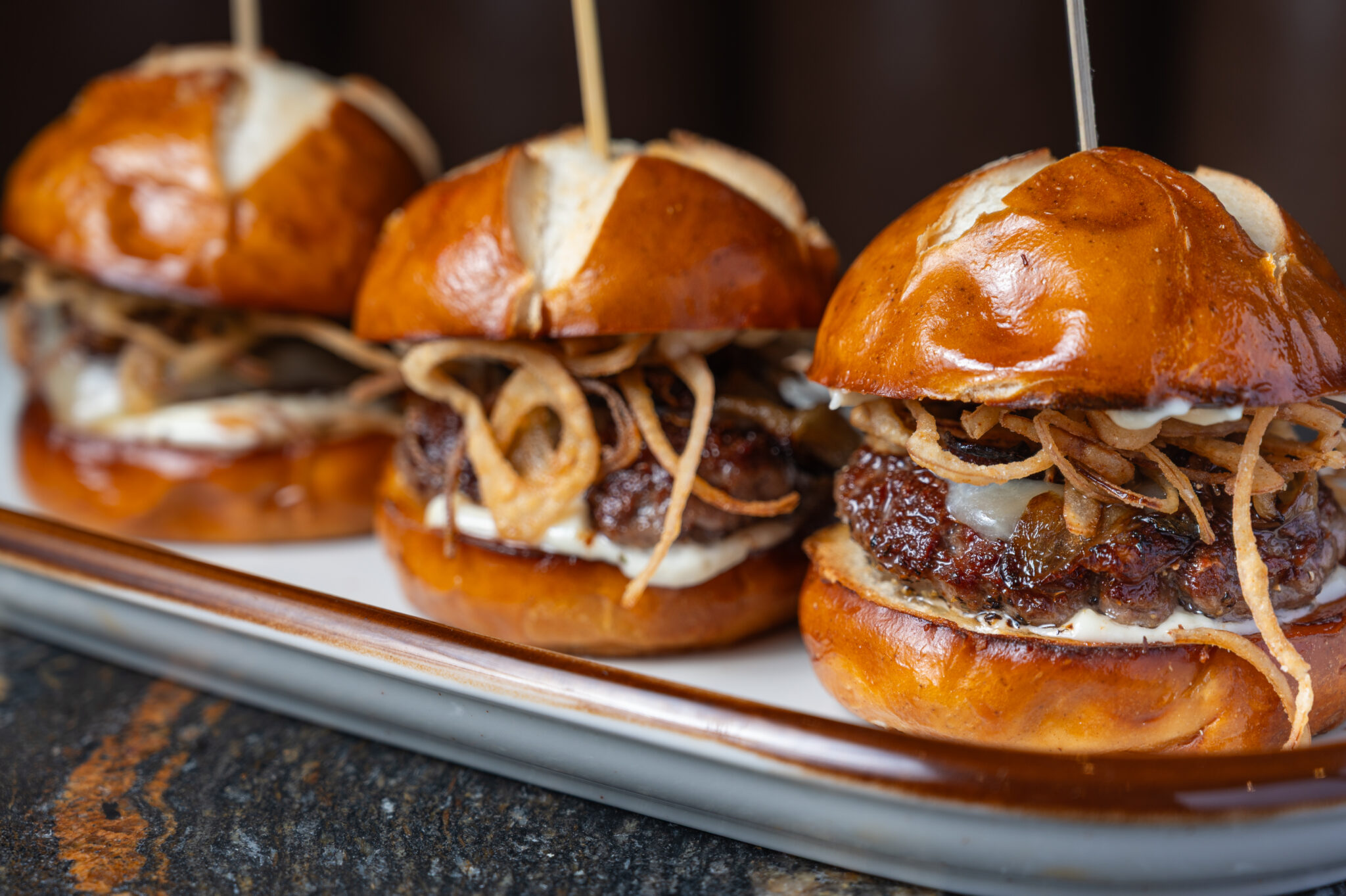 Gourmet beef sliders on pretzel buns served on a wooden board at The Bridewell Tavern