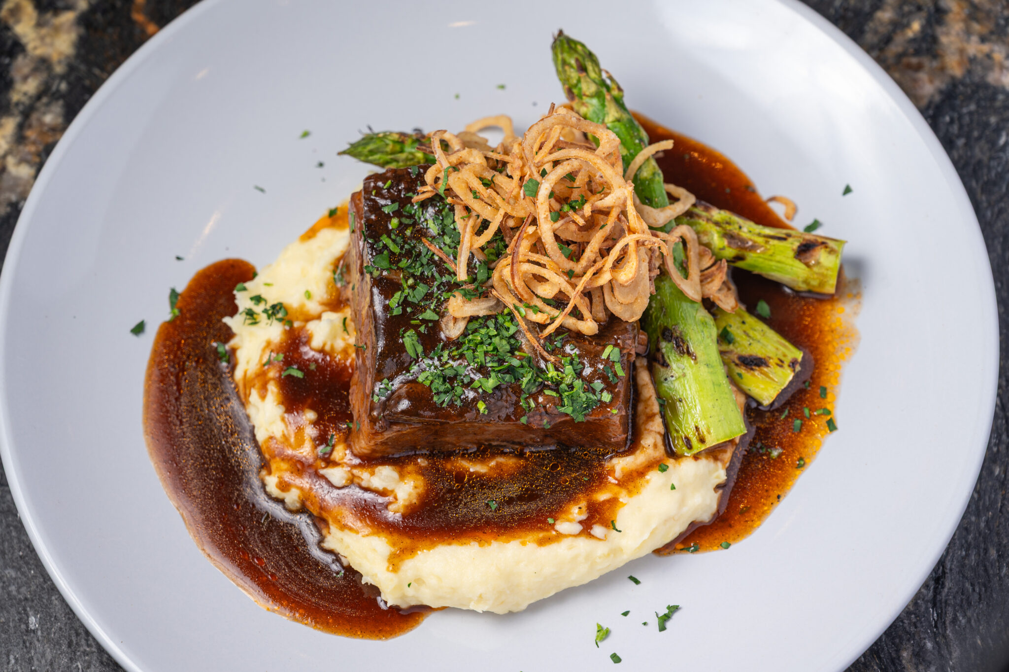 Plated steak with mashed potatoes, asparagus, and crispy onion strings at The Bridewell Tavern