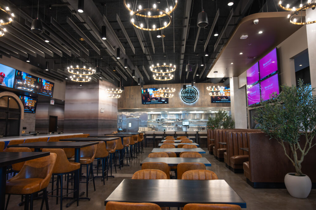 Spacious dining room interior with pendant chandeliers, leather bar chairs, and open kitchen at The Bridewell Tavern