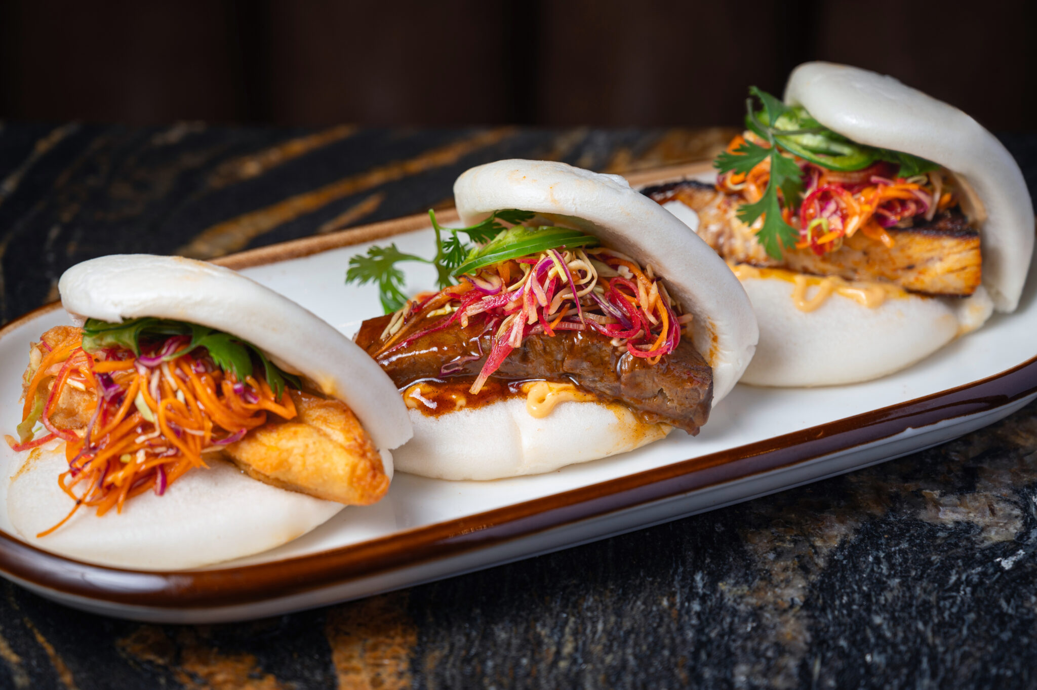 Steamed bao buns filled with braised pork belly and crispy shrimp, topped with pickled slaw, cilantro and jalapeno