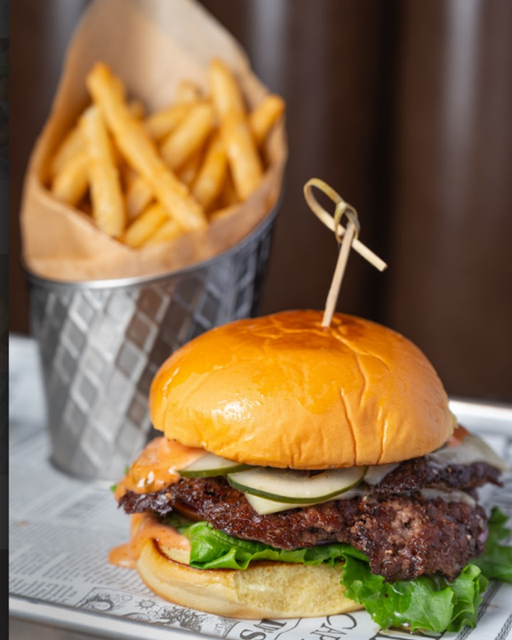 Smash burger with melted cheese, pickles and lettuce on a toasted bun with a bucket of fries