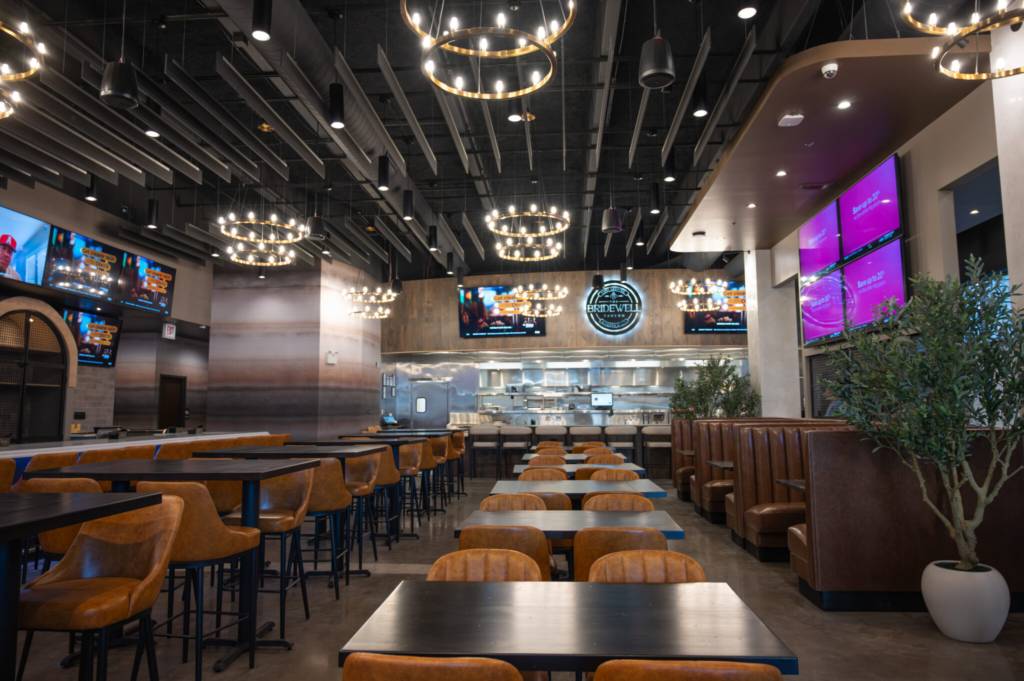 The dining room at The Bridewell Tavern in Burr Ridge with leather booths, ring chandeliers and big screens above the open kitchen